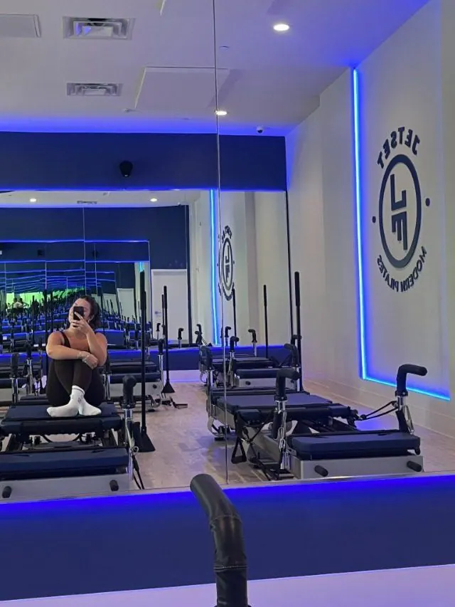Creator sitting on a reformer in a pilates studio lit with blue accent lights