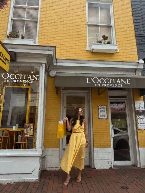 Creator in a yellow dress holding a shopping bag outside the yellow L'Occitane storefront