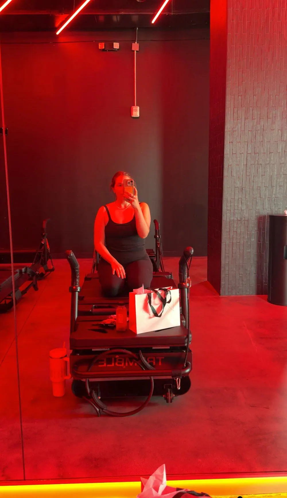 Creator kneeling on a reformer for a mirror selfie under red studio light