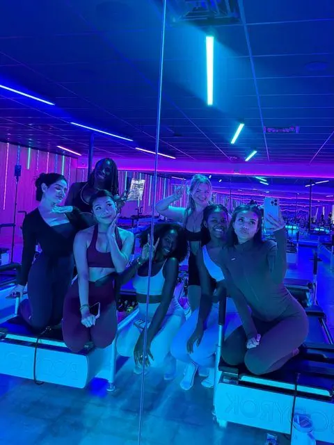 Group of creators posing together on reformers under blue and pink studio lights