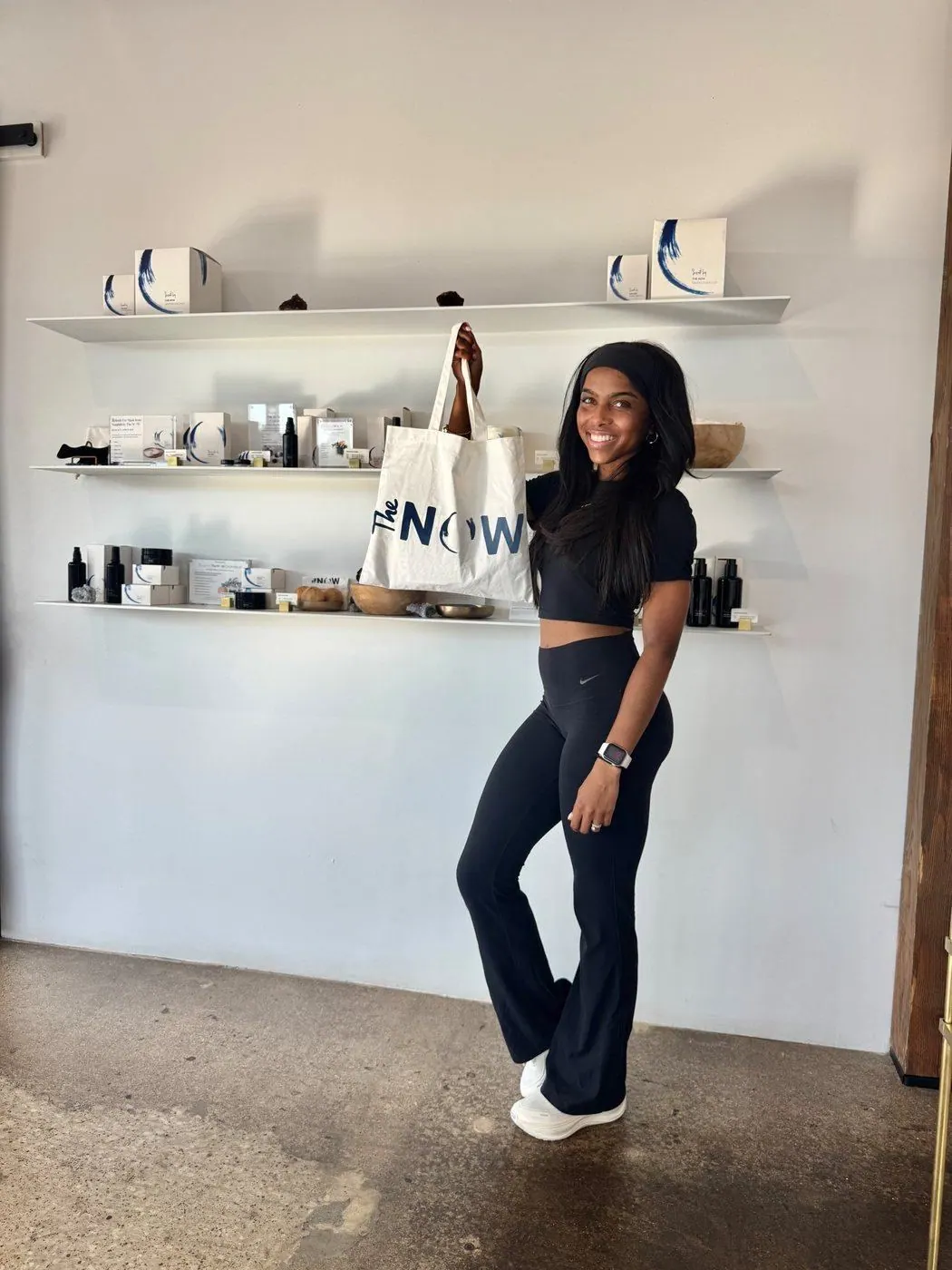 Creator holding up a The NOW Massage tote beside shelves of products