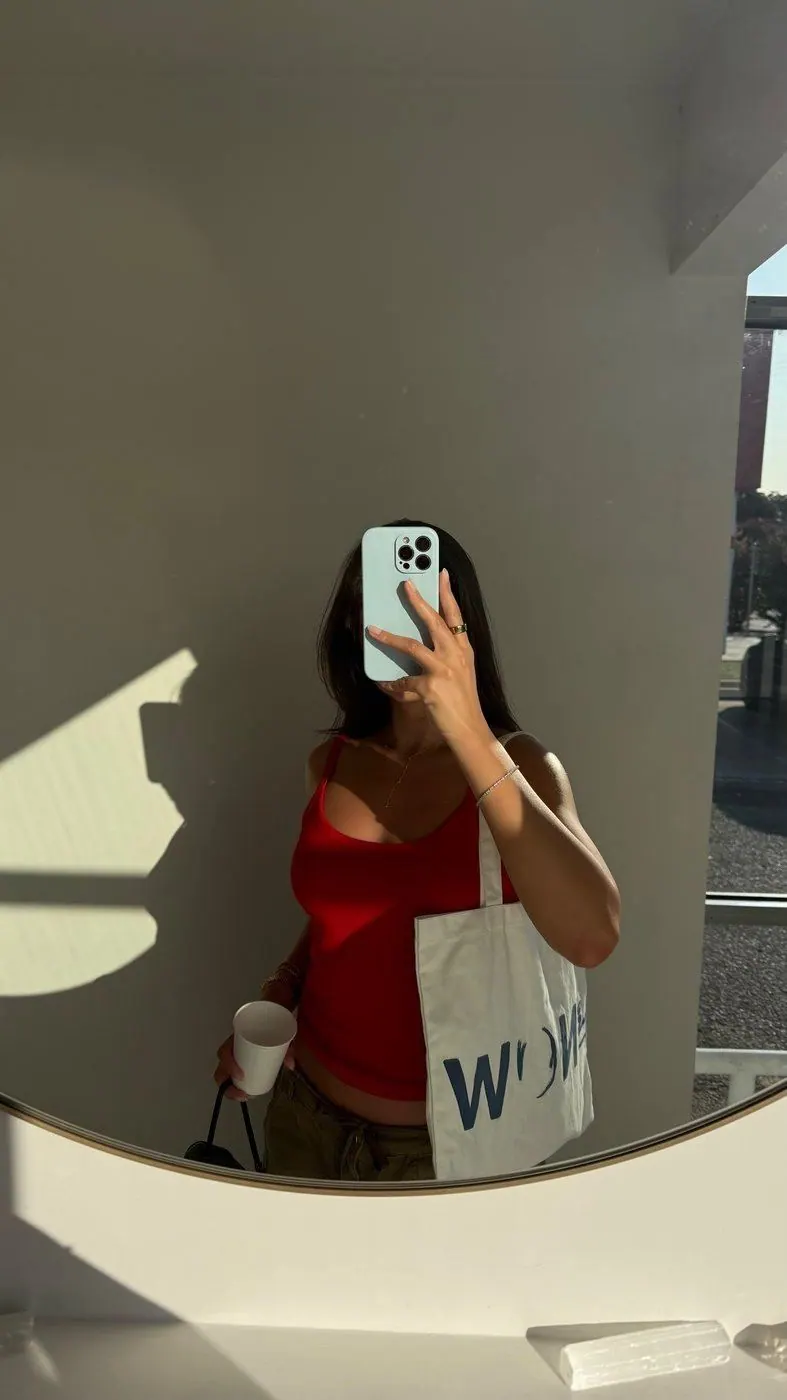 Creator in a red top taking a mirror selfie with a The NOW Massage tote