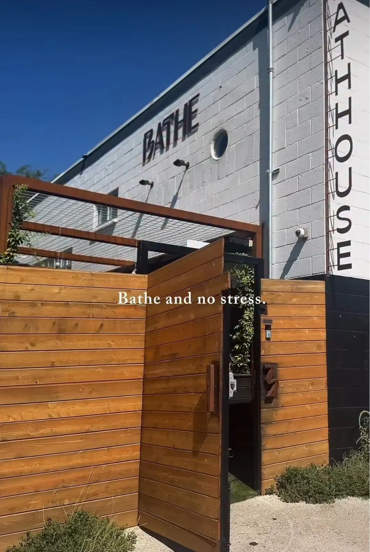 BATHE bathhouse exterior with its sign on white brick and a wooden gate