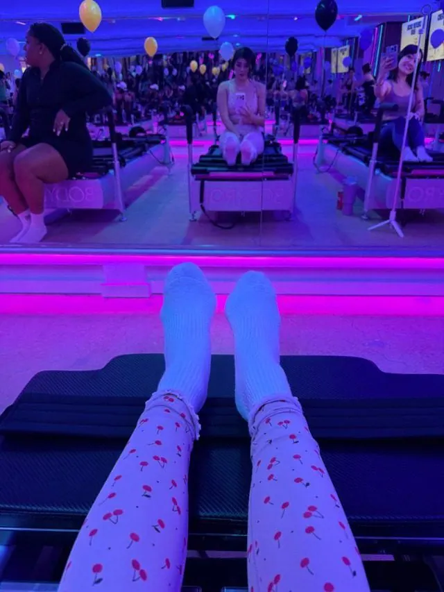 View from a reformer of cherry-print leggings, with balloons and the class reflected in the mirror