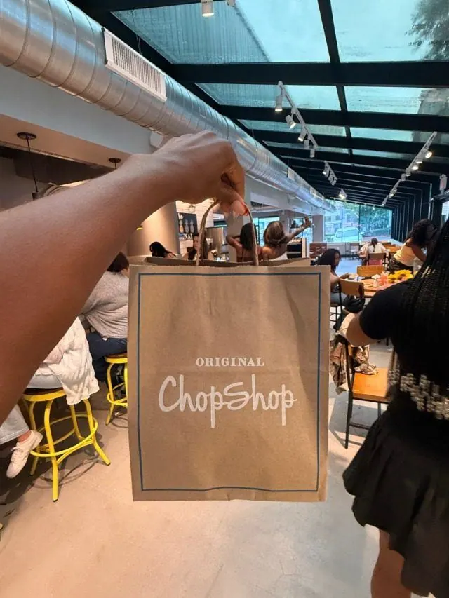 Hand holding up an Original ChopShop bag in a bright, busy dining room